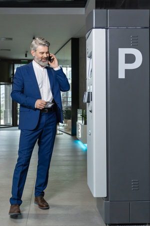 Good-looking tall caucasian man in a nice suit talking on the phone in the business center corridorの写真素材