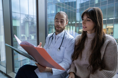 Male doctor in hospital clinic wearing medical uniform reviewing papers with patientの写真素材