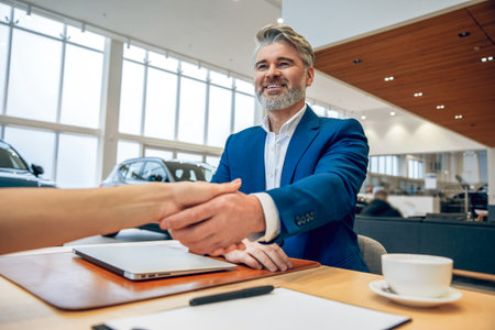 Car rental manager in showroom sitting at table handshaking with customerの写真素材