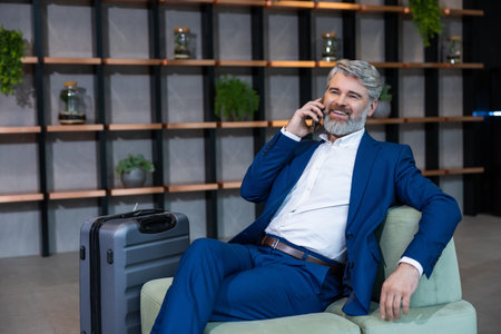 Good-looking well-dressed bearded man sitting in the chair and talking on the phoneの写真素材