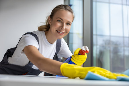 Young woman in yellow gloves cleaning the table in the officeの写真素材