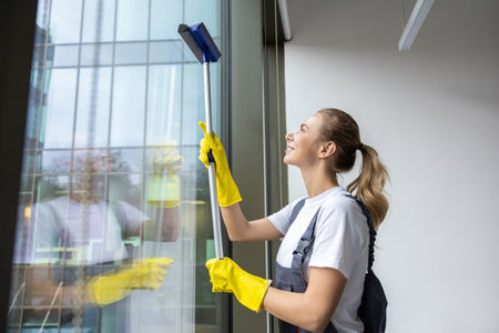 Young woman from cleaning team cleaning the window in the officeの写真素材