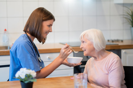 Smiling woman nurse feeding soup to patient in hospitalの写真素材