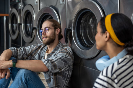 Man and woman waiting together in laundromat, communicating while washing their clothesの写真素材