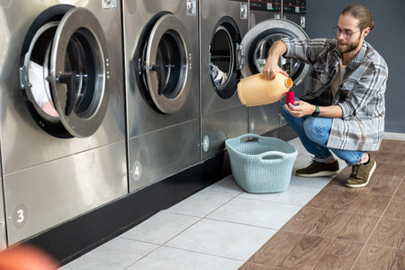 Man in commercial laundry store using detergent in automatic washer to clean household clothの写真素材