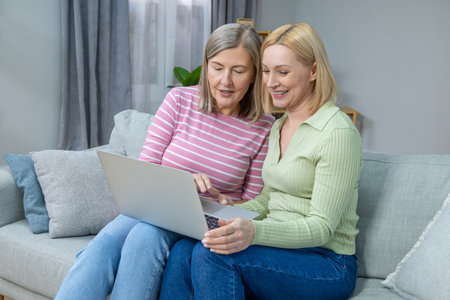 Two women looking old photos on laptop and looking happy and contentedの写真素材