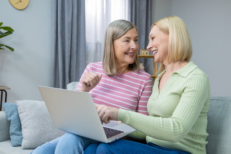 Two women looking old photos on laptop and looking happy and contentedの写真素材