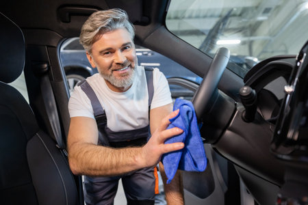 Worker using rag to wipe down dirty transport in garage after repair workの写真素材