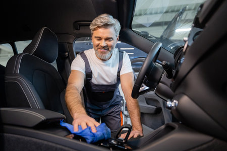 Bearded man worker cleaning automobile salon with ragの写真素材