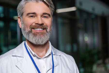 Smiling positive male doctor in lab coat looking contentedの写真素材