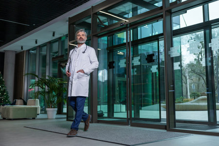 Mature male doctor in lab coat entering the clinic and looking determinedの写真素材