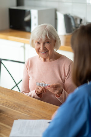In-home nurse assisting senior patient with taking pills for disease treatmentの写真素材