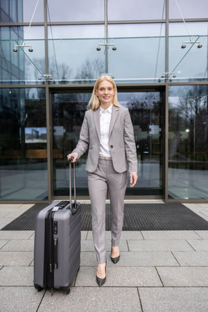 Confident businesswoman walking with suitcase during departure for corporate trip in cityの写真素材
