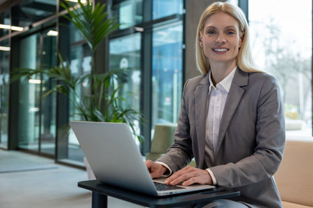 Businesswoman sitting on sofa typing on laptop while working online in officeの写真素材