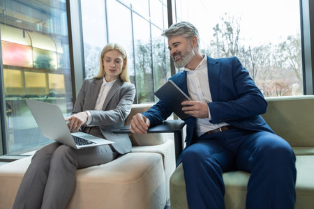Business partners communicating sitting on sofa for professional discussion using laptopの写真素材