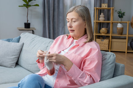 Woman in pink shirt sitting on the sofa and knittingの写真素材