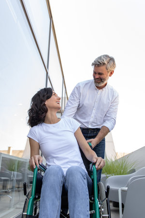 Man carrying a wheelchair of his wife and looking at her with loveの写真素材