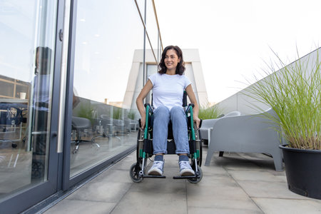 Young dark-haired woman on a wheelchair near the office buildingの写真素材
