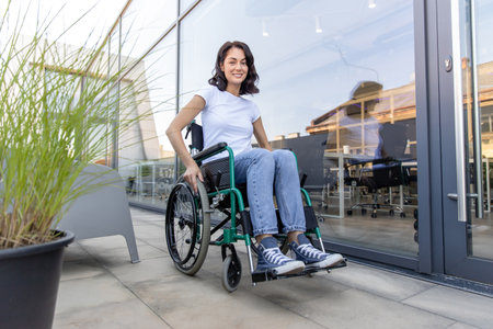 Young dark-haired woman on a wheelchair near the office buildingの写真素材