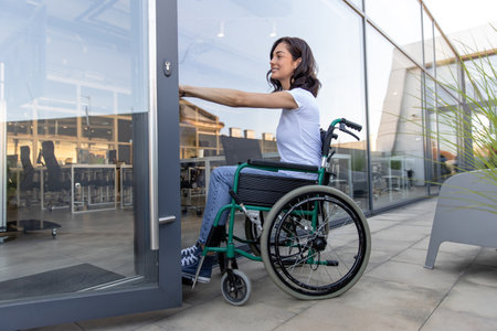 Dark-haired woman on a wheelchair at the office entranceの写真素材