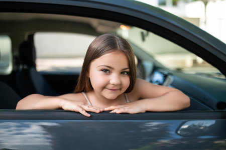 Schoolgirl sitting in car looking out window feeling happy during summer tripの写真素材