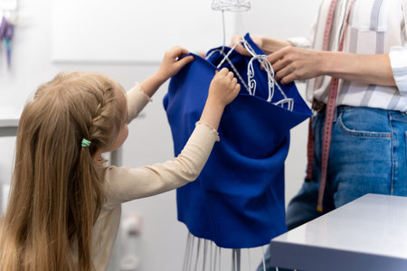 Sweet little girl helping her mom in a sewing salonの写真素材