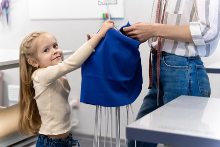 Sweet little girl helping her mom in a sewing salonの写真素材