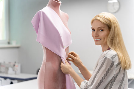 Blonde fashion designer standing near the dummy and trying a new modelの写真素材