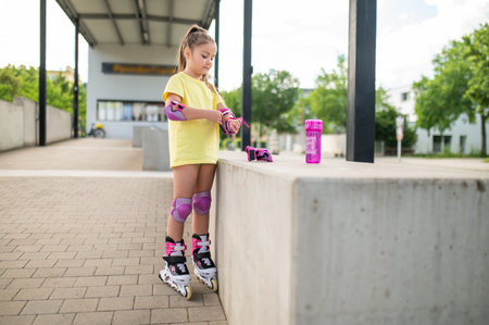 Little female skater adjusting protective gear on hands before skating