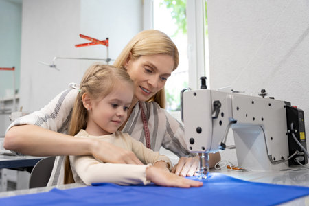 Mom and daughter sitting together at the sewing machine and looking busyの写真素材
