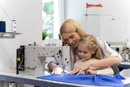Mom and daughter sitting together at the sewing machine and looking busyの写真素材