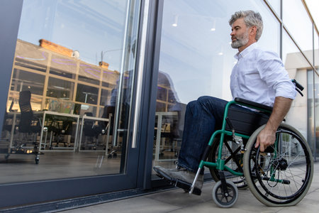 Gray-haired mature man on a wheelchair in the office areaの写真素材