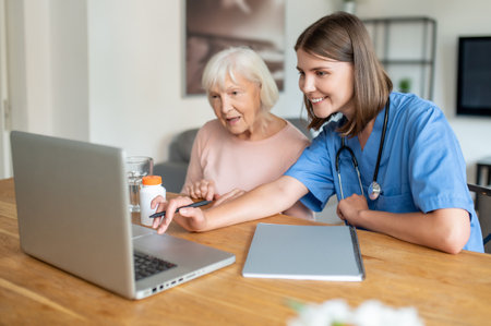 Nurse taking care of disabled senior elderly woman using laptop computer togetherの写真素材