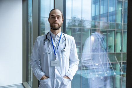 Male young doctor in white lab coat standing near the windowの写真素材