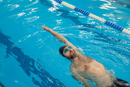 Man in black swimming cap swimming backstroke in the poolの写真素材