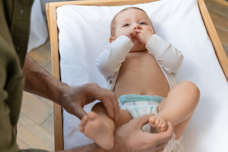 Dad changing a diaper to his little baby boy while the kid smiling and looking happyの写真素材
