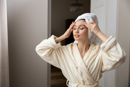 Beautiful woman in white robe gently applies natural facial cleanser to her skinの写真素材