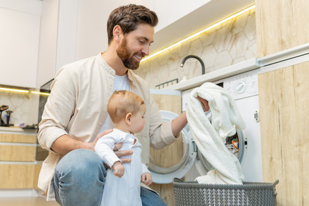 Young man and his little son sorting clothes before putting into washing machineの写真素材