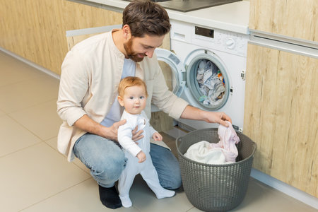 Young man and his little son sorting clothes before putting into washing machineの写真素材