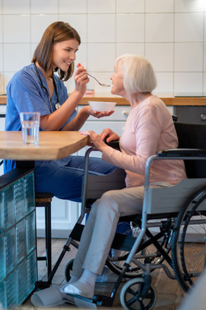 Care assistant feeding elderly lady and both looking contentedの写真素材