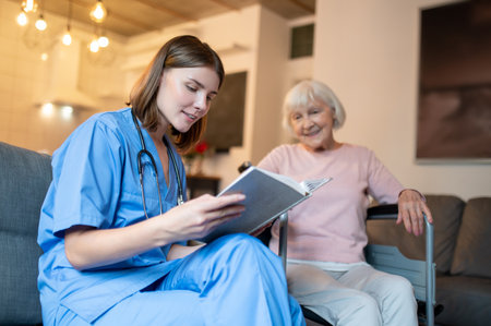Female care assistant reading a book to a elderly lady and both looking enjoyedの写真素材