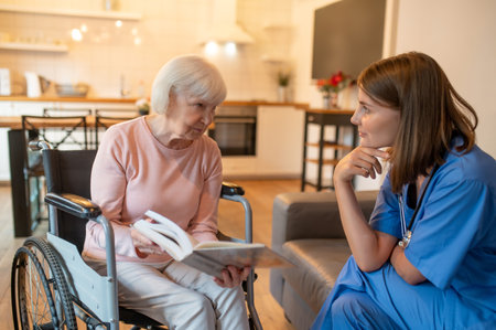 Care assistant with her elderly patient enjoying reading and looking happyの写真素材