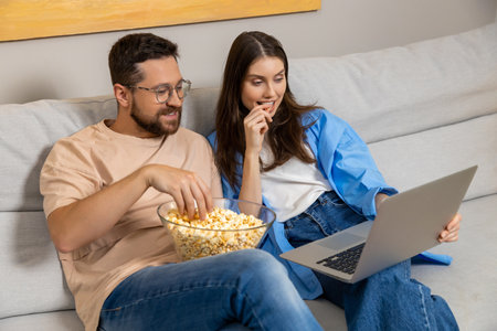 Happy young woman and her boyfriend laughing and eating popcorn from bowl