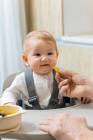 Cute little baby boy sitting in a chair and his dad feeding him