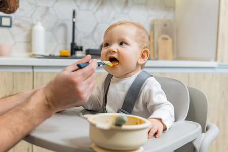 Dad feeding his little baby boy while kid sitting in his chairの写真素材