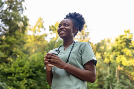 Smiling positive african american nurse having coffee in the parkの写真素材