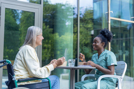 Nurse and female patient having lunch in the clinic yard and looking involvedの写真素材