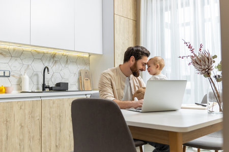 Bearded young caucasian man working from home while taking care of his little sonの写真素材