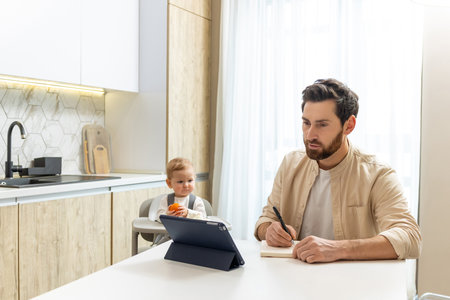 Young father working from home, his baby boy playing next to himの写真素材