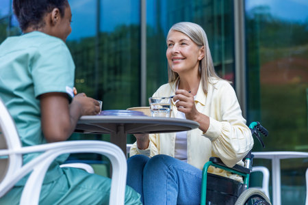 Nurse and a patient on a wheelchair having lunch together and talkingの写真素材